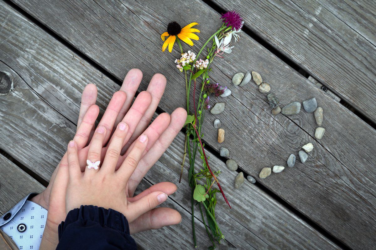 Hände einer Familie mit Blumen und einem Herz aus Steinen geformt
