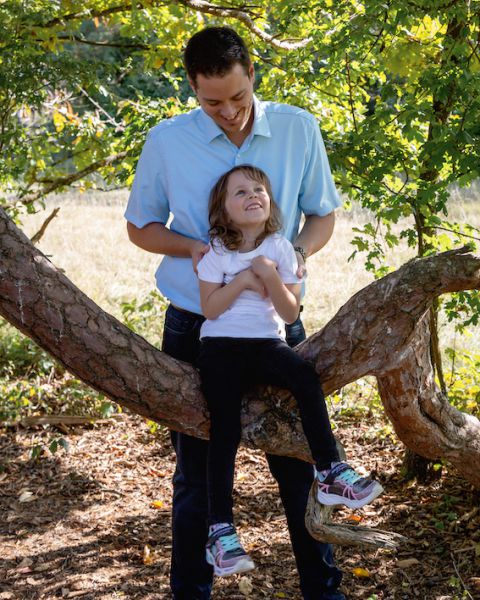 Ein Kind, dass auf einem Ast sitzt und sich an seinen Vater anlehnt