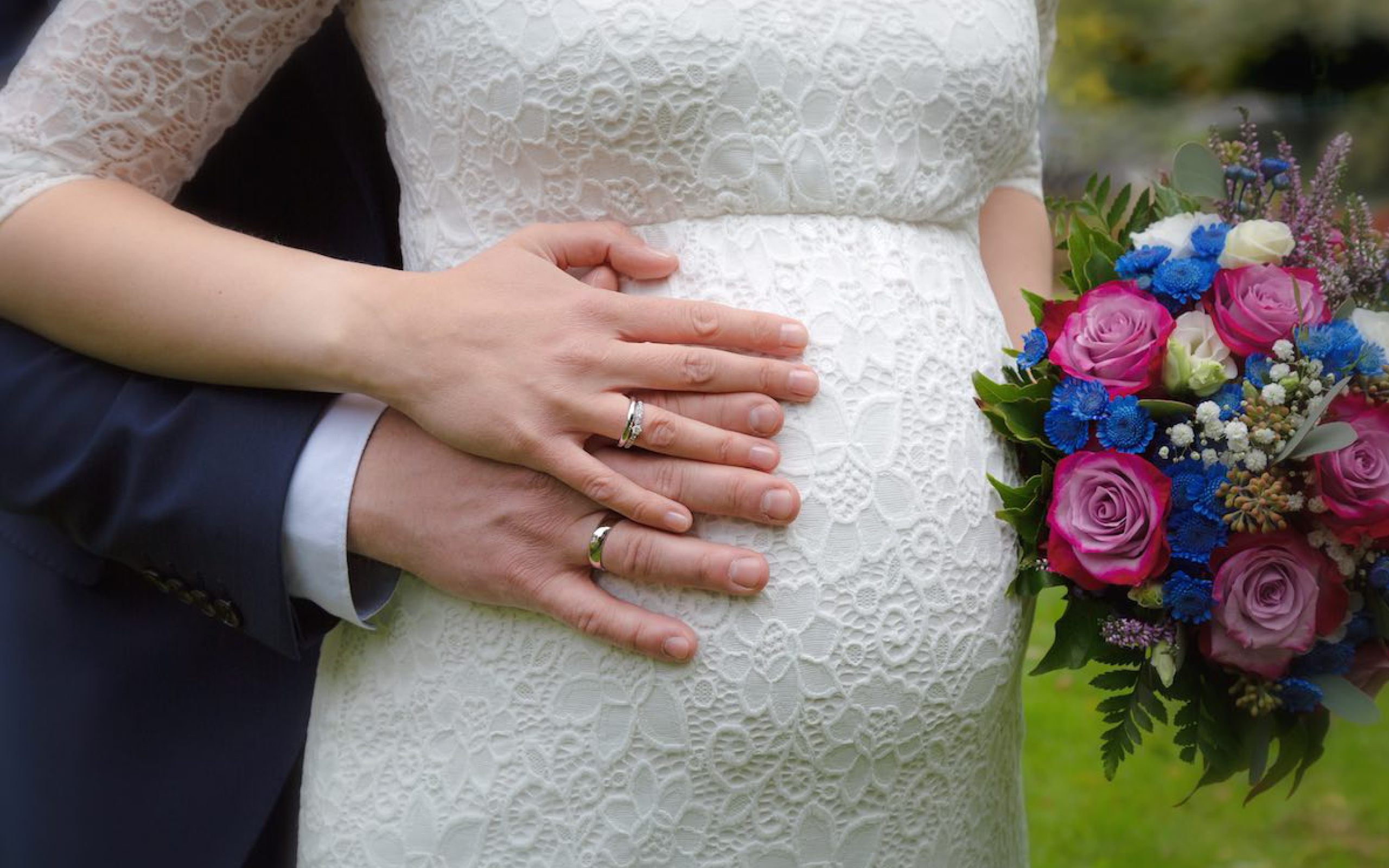 Brautpaar, deren Hände auf dem Babybauch der Braut liegen